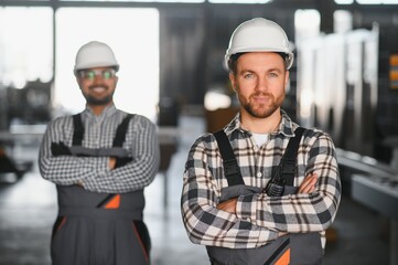 Two male international workers in overalls work together at a machine for the production of aluminum PVC windows and doors