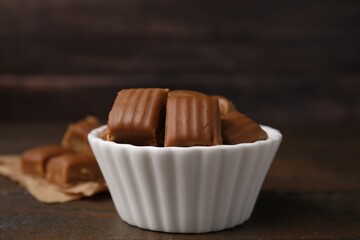 Tasty sweet caramel candies in bowl on wooden table, closeup