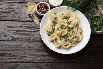 Delicious pelmeni with green onion served on wooden table, flat lay. Space for text