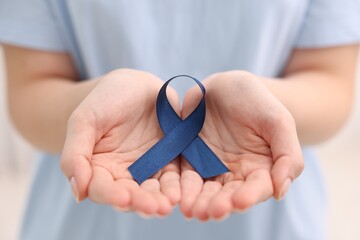 Woman with dark blue ribbon on light background, closeup. Arthritis disease and colon cancer...