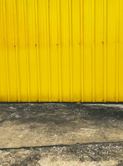 Old metal sheet fence, yellow painted metal sheet wall and weathered ground cement floor, vertical image outdoor background in the city.