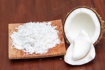 Grated coconut set on wooden board with half cut and pieces of coconut fruit