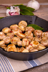 A cast iron skillet filled with sauteed mushrooms. The mushrooms are cooked to perfection with chili flakes, garlic and herbs. A tea towel and rustic wooden background enhances the presentation.
