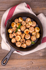 A cast iron skillet filled with sauteed mushrooms. The mushrooms are cooked to perfection with chili flakes. A tea towel and rustic wooden background enhances the presentation.