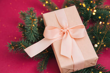 Christmas, festive background. Rose gift box with pink ribon on green coniferous branches on a pink background. Top view