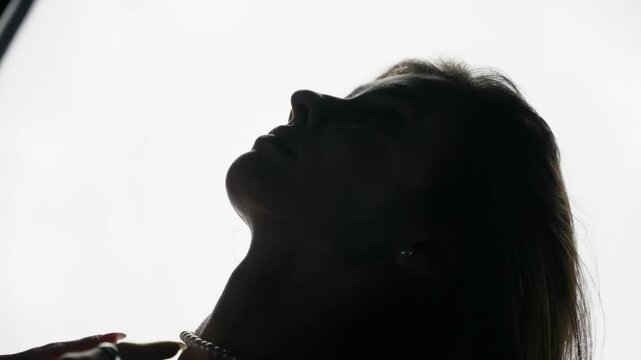 Backlit silhouette of a young woman wearing a pearl necklace, posing on a dark background, slowly revealing her body and sensuality