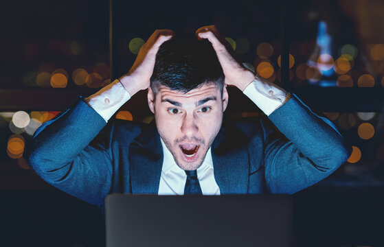 Bad News. Shocked Businessman Shouting Touching Head Looking At Laptop Sitting Overnight In Modern Office.