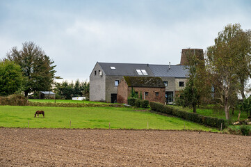 Obraz premium Plowed agriculture fields and farm houses at the Flemish countryside in Boutersem, Flemish Brabant, Belgium