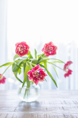 A bouquet of pink tulips, some drooping, rests in a glass vase on a wooden surface
