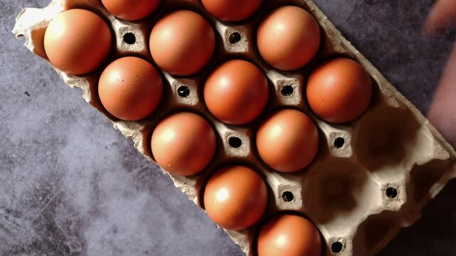 Hands pick eggs from an egg carton or egg stand to use in cooking.