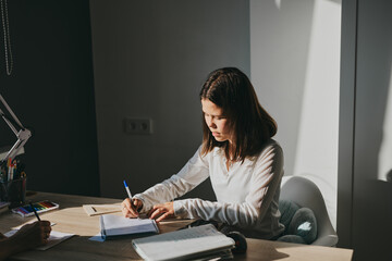 Schoolgirl at home schooling. The girl sits at the table with textbooks doing homework