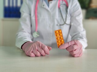 Healthcare professional in gloves holds orange medication pill blister pack
