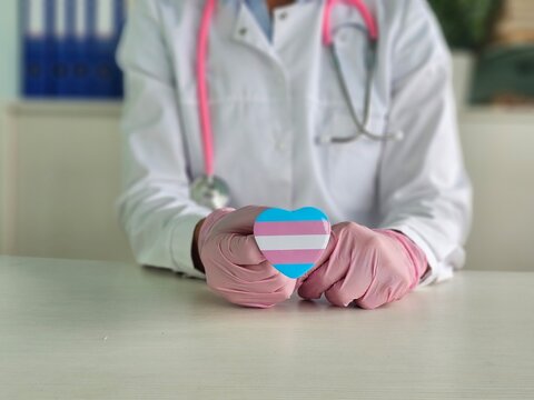 Healthcare professional holds a pink and blue heart symbolizing transgender pride