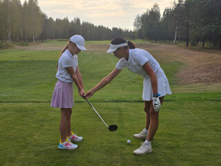 A young girl receives golf training from an instructorat a lush, green golf course