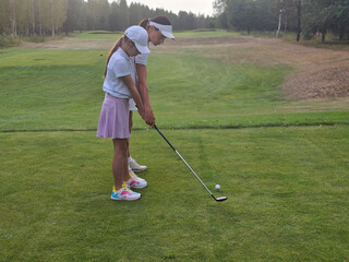 Two young girls practicing their golf swings on a beautiful course during a sunny afternoon