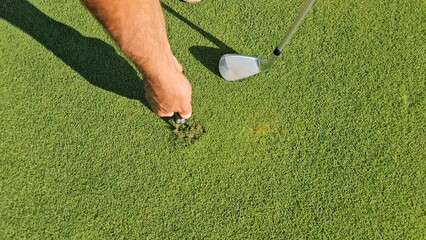A golfer repairs the greens at a single golf course in the afternoon, paying special attention to...