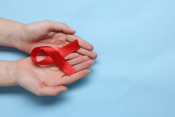 Woman with red ribbon on light blue background, top view and space for text. HIV (AIDS) disease awareness