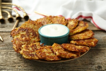 Delicious potato pancakes, sour cream, menorah and candles on wooden table, closeup. Hanukkah festive food