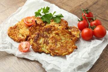 Delicious potato pancakes, tomatoes and parsley on wooden table, closeup