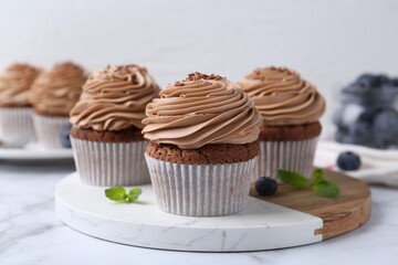 Tasty cupcakes with chocolate cream and blueberries on white marble table, closeup