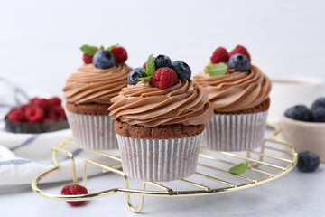 Tasty cupcakes with chocolate cream and berries on white table, closeup
