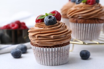 Tasty cupcakes with chocolate cream and berries on white table, closeup