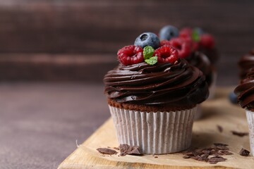 Tasty cupcakes with chocolate cream and berries on brown table, closeup. Space for text