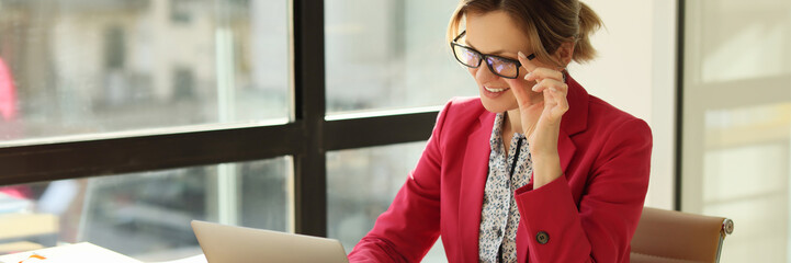 Positive woman takes off glasses with hand looking at screen
