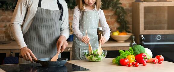 Loving father teaching little girl how to cook healthy food, making vegetable salad in kitchen together