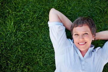Woman, portrait and smile on grass space for relax, peace and positive mental health. Above, mature person and happy in nature park for summer, travel freedom and stressless environment for wellness