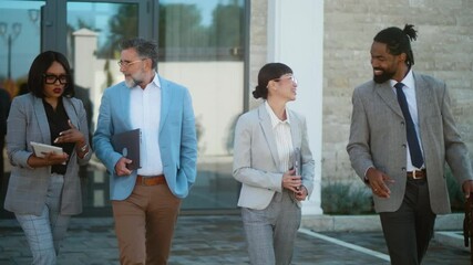 Cheerful multiracial group of business people exiting an office building and communicating while leaving work