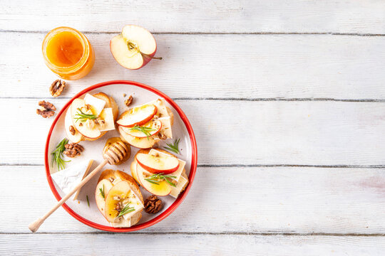 Autumn Apple Brie Crostini with Walnuts and Honey, Fall dinner, Thanksgiving party appetizers idea. Small sandwiches with red apple slices, brie cheese and sweet honey drizzles - Powered by Adobe