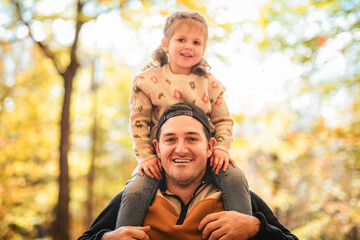 Fototapeta premium Joyful dad and his little daughter. daddy and child have fun, laugh and enjoy nature outdoors at autumn park.