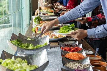 Hands of a young Asian women are selecting salad ingredients at buffet restaurant.