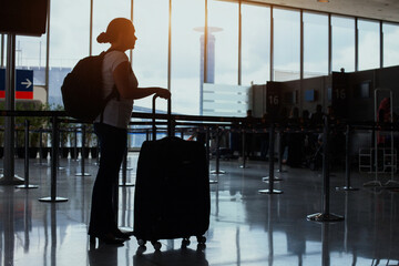 airport check-in and baggage drop-off counter, woman waiting with luggage, passenger silhouette