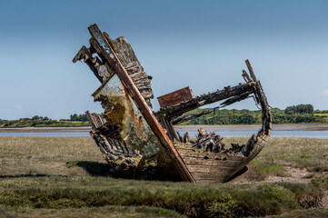 Old wooden fishing boat by river with grass and blue sky in background, shipwreck, ships graveyard,...