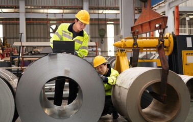 Two male engineers in uniforms and caps using laptop checking machinery system in factory. Industrial factory workers. Machinery maintenance technician working concept.