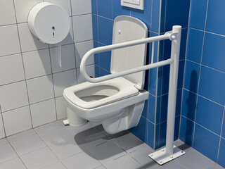 A close-up of a white toilet in a blue and white tiled restroom equipped with a handrail for...