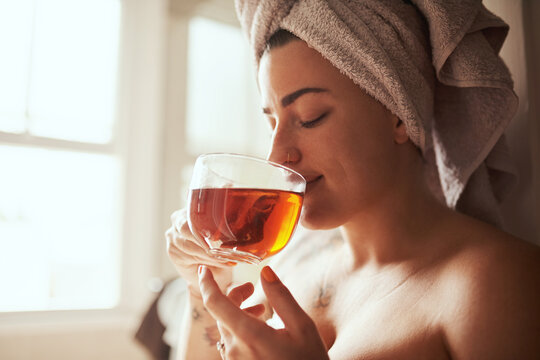 Woman, relax and drinking with tea for morning routine, hygiene or cleanse in bathroom at home spa. Young, female person or window with beverage for calm breakfast, detox or peaceful day at house