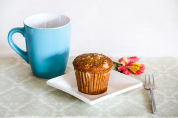 Close Up of a Hot Blue Cup of Coffee, Tea, Milk or Chocolate with a Coconut Muffin with Nut Slices on a White Plate near a Fork with a Flower on the Background. Bakery Isolated. Coffee Break Concept. 