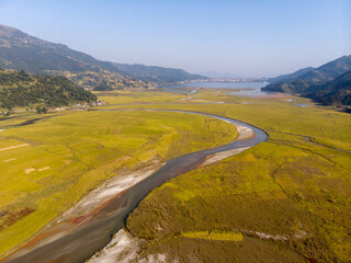 Aerial view of a meandering river flowing through a vast, green valley surrounded by mountains.