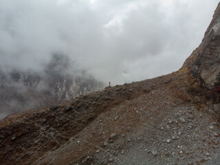 A lone figure stands atop a rugged mountain ridge, surrounded by mist and stunning natural scenery.