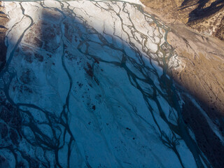 A breathtaking bird's-eye view of a glacial river system on a snowy mountain slope.