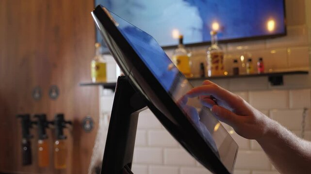 A close-up of a waiter or bartender working at a computer in a cafe, he clicks on the touch screen and places an order. The waiter works with an electronic panel for orders and receipts.