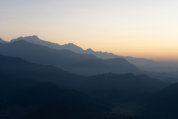 Fototapeta premium A serene mountain landscape at dawn with layers of mist and a warm, glowing horizon.