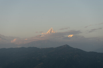 A serene view of a mountain peak at dusk, with a layer of clouds and a fading horizon.