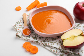 Delicious baby food in bowl and ingredients on white table