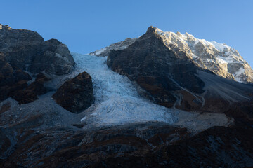 A rugged mountain landscape with a glacier cascading down its rocky slopes.
