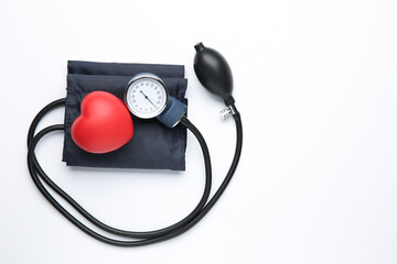 Blood pressure measuring device and red decorative heart on light background, top view. Space for...