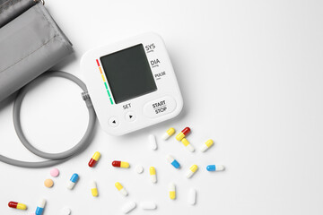 Blood pressure measuring device and pills on white background, top view. Space for text